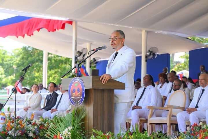 Le Premier ministre Alix Didier Fils-Aimé prononce un discours lors d'une cérémonie officielle à la Primature, vêtu de blanc, devant des membres du gouvernement haïtien. © Primature / Presslakay