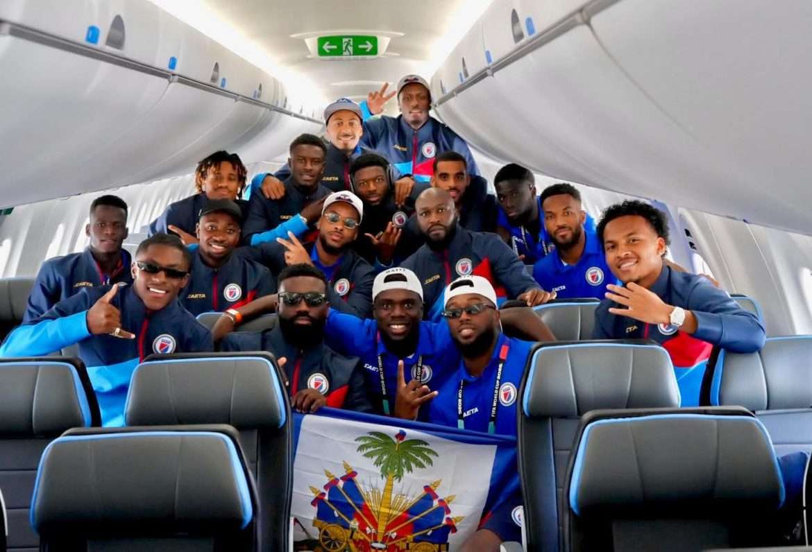 Les joueurs de la sélection nationale haïtienne posent avec le drapeau d'Haïti à bord de l'avion qui les transporte vers leur camp de base de Stockton University, dans le New Jersey, le 8 juin 2026. Les Grenadiers disputeront leur premier match du Groupe C face au Maroc le 13 juin prochain, dans le cadre de la Coupe du monde FIFA 2026.