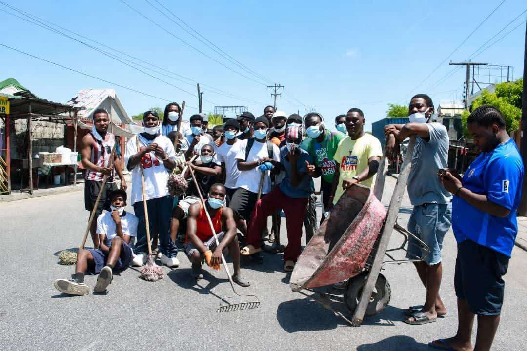 Un groupe de jeunes de L'Estère posent avec balais, râteaux et brouette après le nettoyage des rues de la ville, le 1er août 2026.